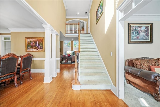 staircase with ornamental molding, wood finished floors, decorative columns, and baseboards