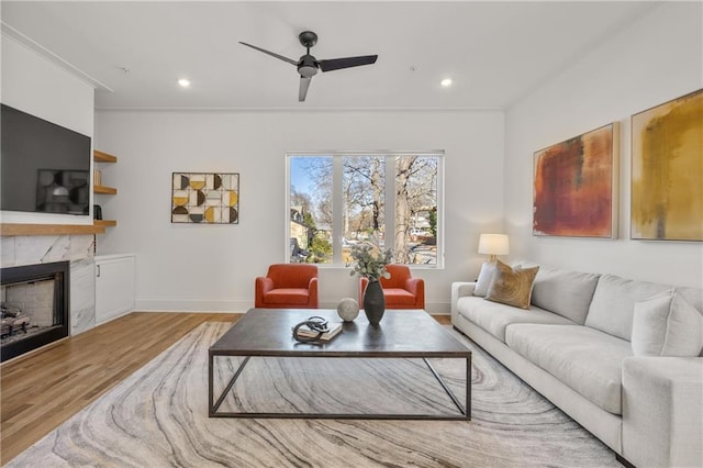 living room with a high end fireplace, light hardwood / wood-style flooring, and ceiling fan