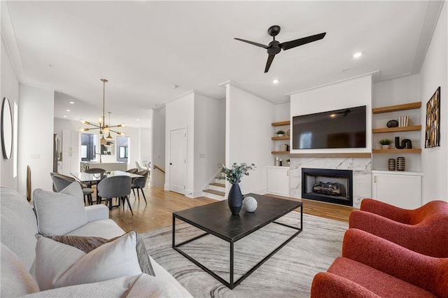 living room featuring ceiling fan with notable chandelier, a fireplace, light hardwood / wood-style floors, and crown molding