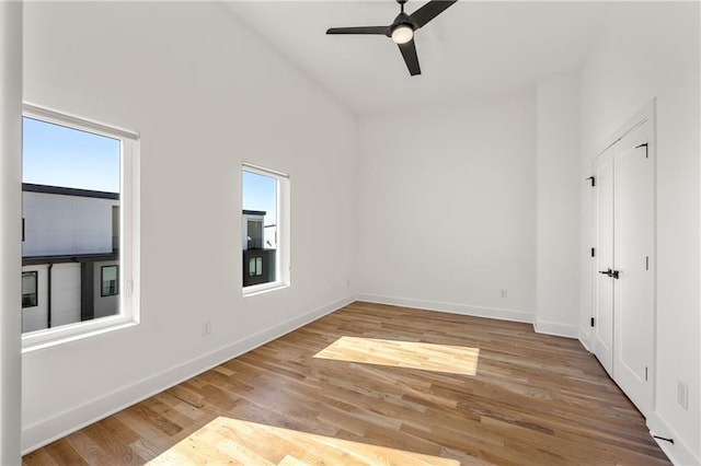 empty room featuring ceiling fan, a towering ceiling, and light hardwood / wood-style floors