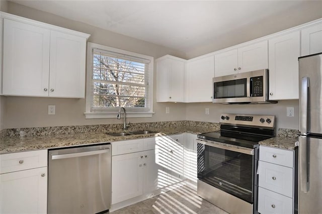 kitchen with light stone countertops, appliances with stainless steel finishes, white cabinetry, and sink