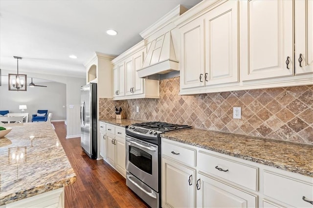 kitchen with hanging light fixtures, stainless steel appliances, ornamental molding, custom range hood, and light stone countertops