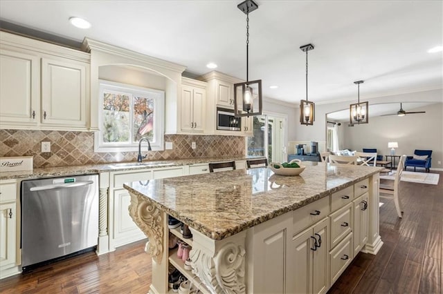 kitchen with sink, hanging light fixtures, stainless steel appliances, light stone counters, and a kitchen island