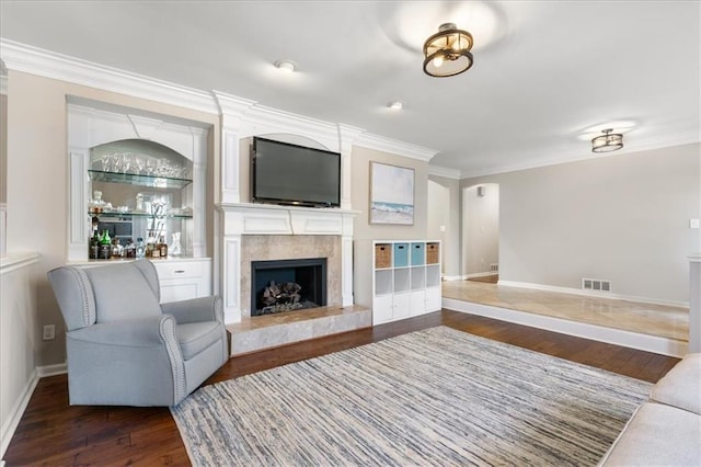 living room with crown molding, indoor bar, a premium fireplace, and dark hardwood / wood-style floors