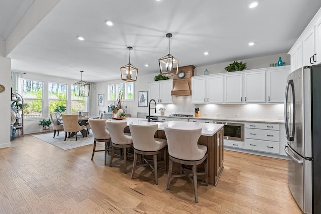 kitchen featuring light wood-style floors, stainless steel appliances, custom exhaust hood, and backsplash