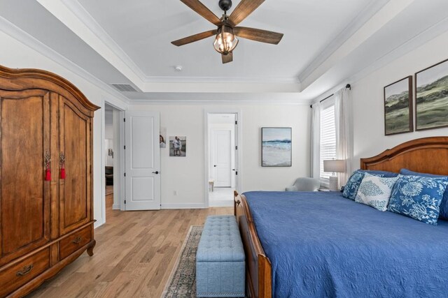 bedroom featuring visible vents, baseboards, crown molding, light wood finished floors, and a raised ceiling