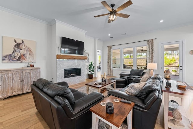 living room with light wood finished floors, a glass covered fireplace, plenty of natural light, and crown molding