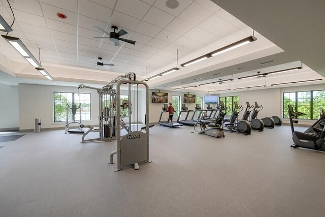 workout area featuring ceiling fan, baseboards, and a tray ceiling