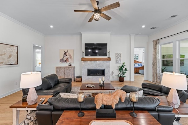 living area with visible vents, a healthy amount of sunlight, ornamental molding, wood finished floors, and a glass covered fireplace