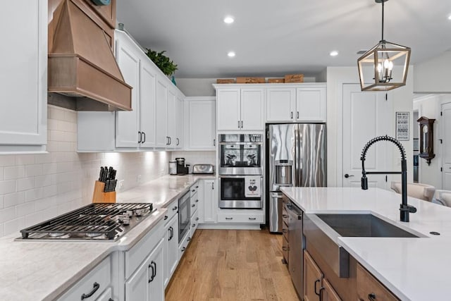 kitchen with premium range hood, appliances with stainless steel finishes, light wood-style floors, white cabinets, and a sink