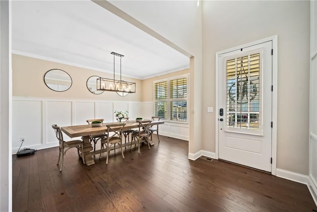 dining space featuring a notable chandelier, dark wood-type flooring, ornamental molding, wainscoting, and a decorative wall