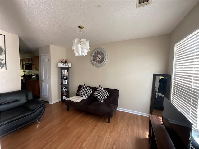 living room featuring a chandelier, visible vents, light wood-style flooring, and a textured ceiling