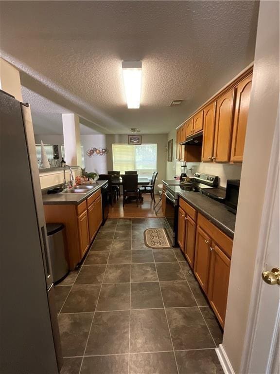 kitchen with appliances with stainless steel finishes, dark tile patterned floors, dark countertops, and a sink