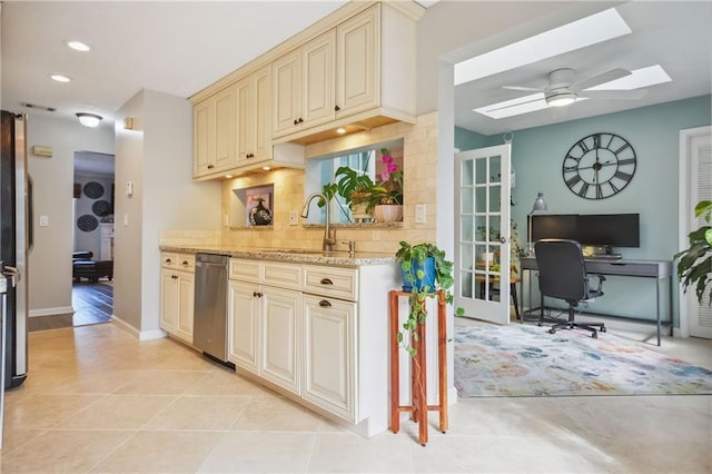 kitchen with sink, backsplash, cream cabinetry, light stone counters, and a skylight