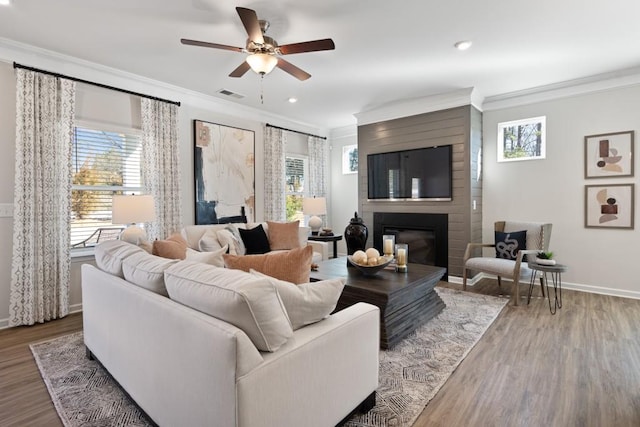 living room featuring a large fireplace, hardwood / wood-style flooring, ceiling fan, and crown molding