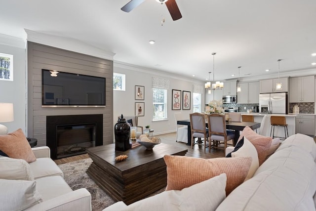 living room with ceiling fan, a large fireplace, wood-type flooring, and ornamental molding