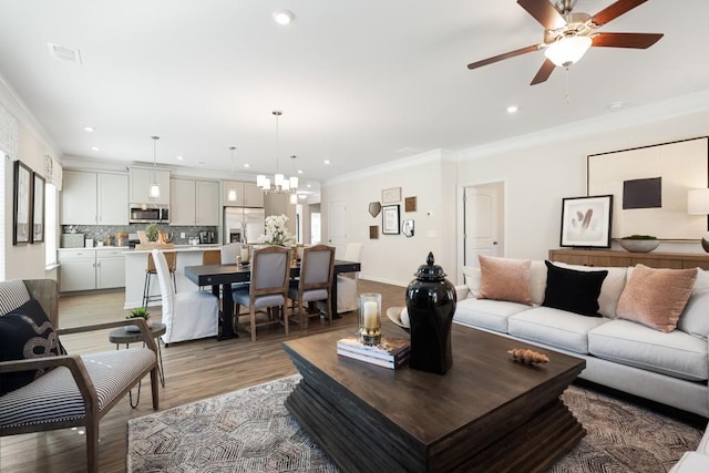 living room with crown molding, light hardwood / wood-style floors, and ceiling fan with notable chandelier