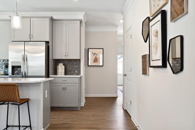 kitchen featuring backsplash, hanging light fixtures, gray cabinets, stainless steel fridge, and a breakfast bar area