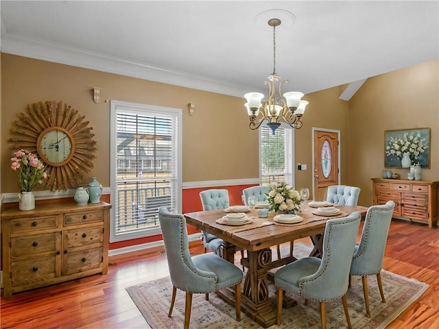 dining space with lofted ceiling, a notable chandelier, crown molding, and light hardwood / wood-style flooring