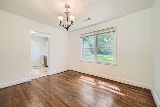 unfurnished room featuring a textured ceiling, dark hardwood / wood-style floors, and a notable chandelier