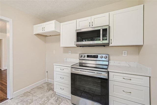 kitchen featuring a textured ceiling, stainless steel appliances, white cabinetry, and light stone counters