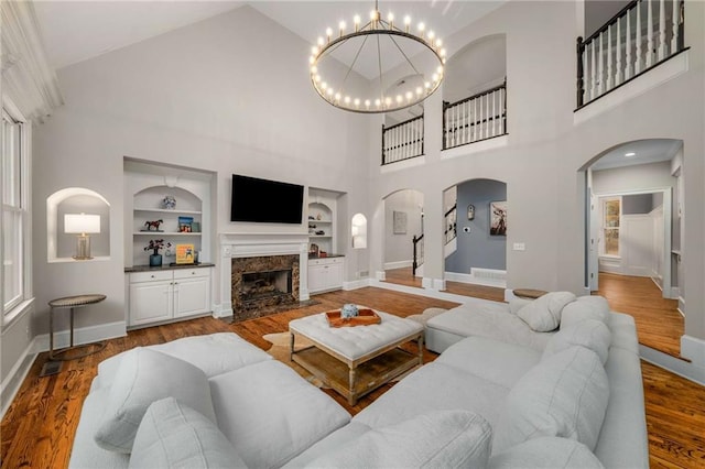 living room with a wealth of natural light, hardwood / wood-style flooring, a notable chandelier, a high end fireplace, and built in shelves