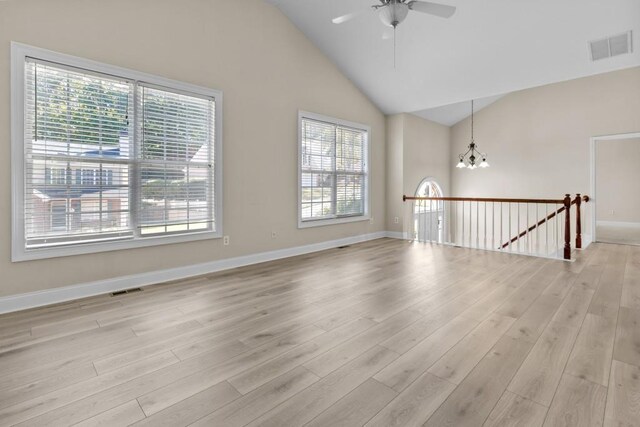 unfurnished living room with high vaulted ceiling, light hardwood / wood-style floors, ceiling fan with notable chandelier, and a wealth of natural light