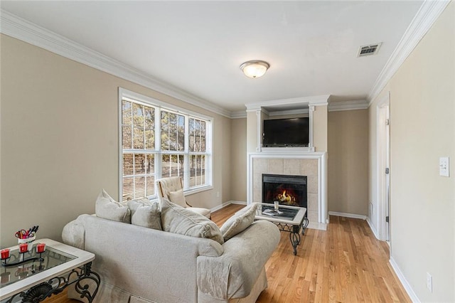 living room with light hardwood / wood-style floors, crown molding, and a tiled fireplace