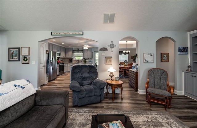 living room featuring arched walkways, a textured ceiling, visible vents, ceiling fan with notable chandelier, and wood finished floors