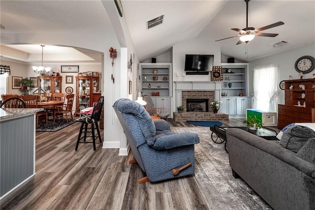 living area with a brick fireplace, wood finished floors, visible vents, and ceiling fan with notable chandelier