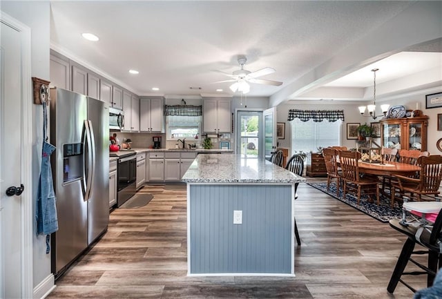 kitchen with a sink, ceiling fan with notable chandelier, light stone countertops, appliances with stainless steel finishes, and gray cabinetry