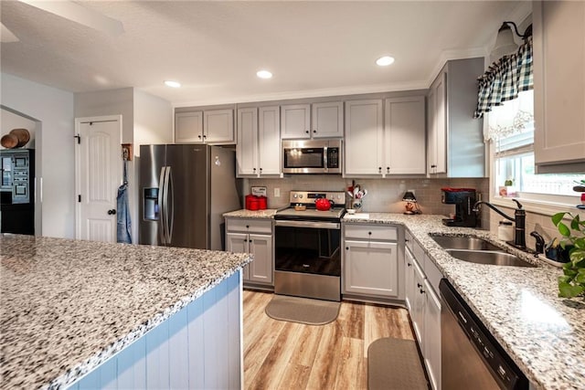 kitchen featuring light wood-style flooring, light stone countertops, appliances with stainless steel finishes, and a sink