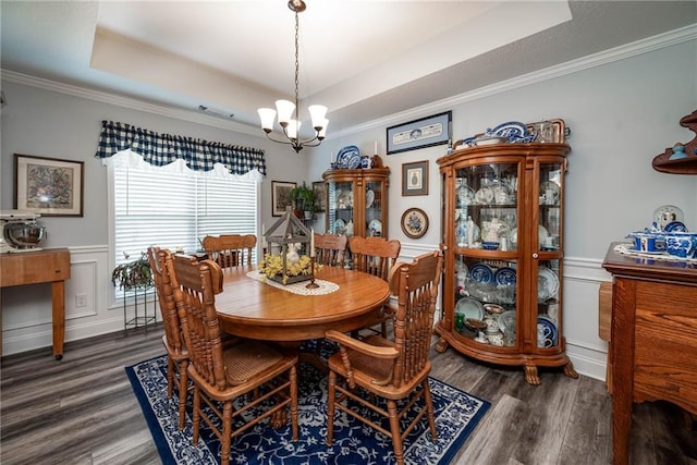 dining room featuring a raised ceiling, wainscoting, an inviting chandelier, wood finished floors, and ornamental molding
