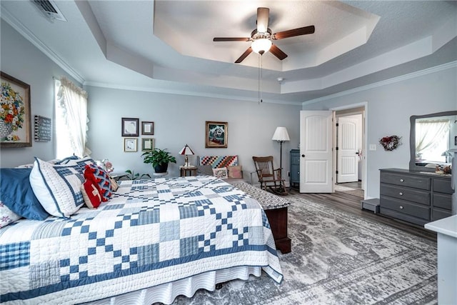 bedroom with a tray ceiling, visible vents, a ceiling fan, wood finished floors, and crown molding