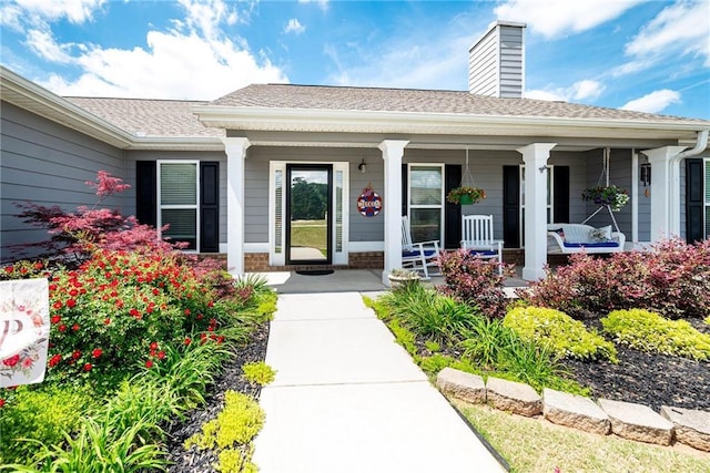 doorway to property with a shingled roof, a chimney, and covered porch
