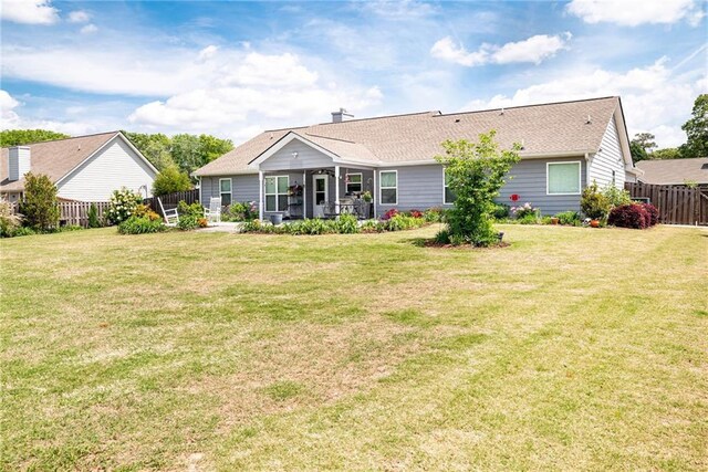back of property featuring a lawn, a shingled roof, and fence