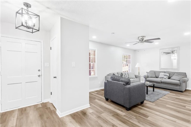 living room featuring ceiling fan with notable chandelier and light wood-type flooring