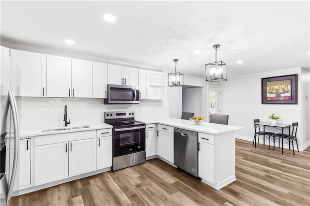 kitchen with kitchen peninsula, light hardwood / wood-style floors, decorative light fixtures, white cabinets, and appliances with stainless steel finishes