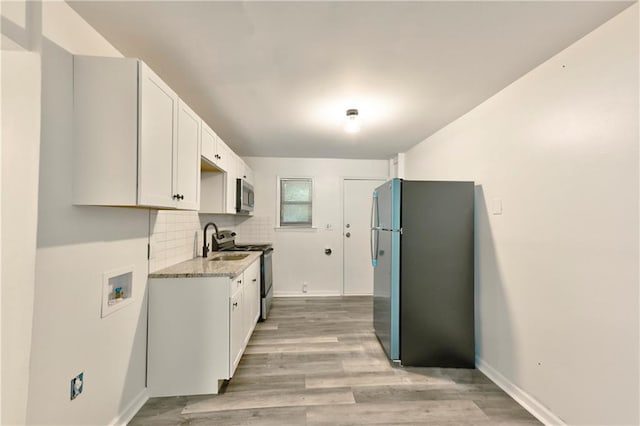 kitchen with stainless steel appliances, white cabinetry, baseboards, backsplash, and light wood finished floors