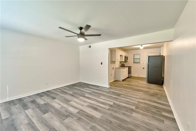 unfurnished living room with light wood finished floors, visible vents, baseboards, ceiling fan, and a sink