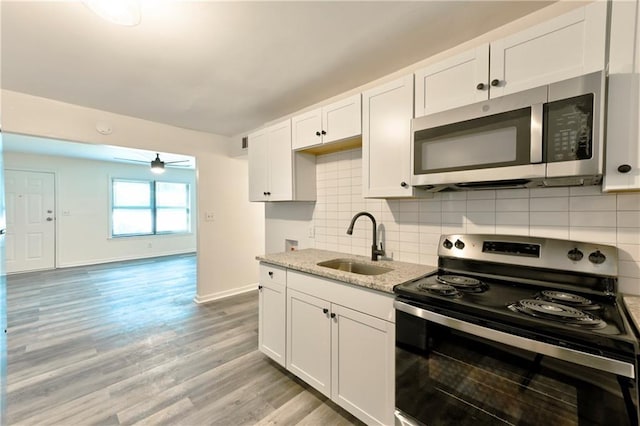 kitchen featuring light wood finished floors, decorative backsplash, light stone counters, stainless steel appliances, and a sink