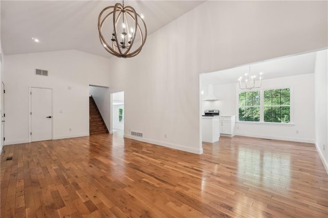 unfurnished living room with an inviting chandelier, light hardwood / wood-style flooring, and high vaulted ceiling