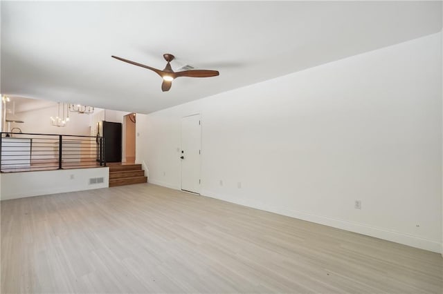 unfurnished living room with ceiling fan with notable chandelier and light hardwood / wood-style flooring