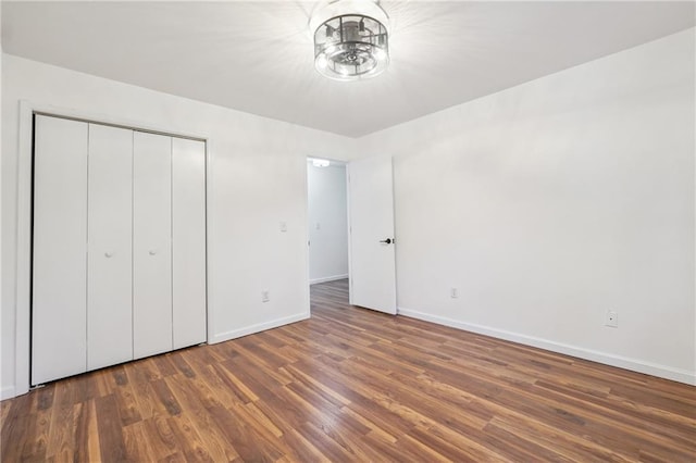 unfurnished bedroom with dark wood-type flooring, an inviting chandelier, and a closet