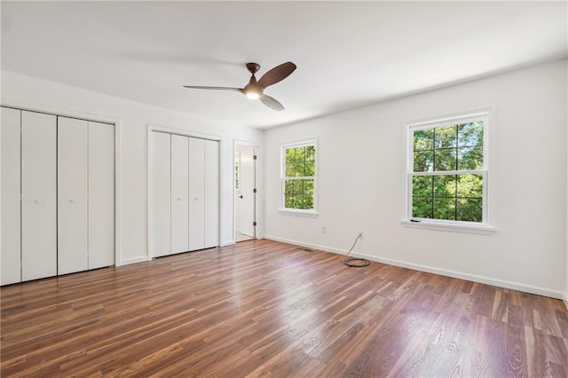 unfurnished bedroom featuring ceiling fan, dark hardwood / wood-style floors, and multiple closets