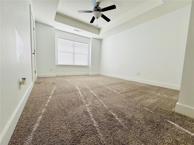 carpeted spare room featuring a tray ceiling, ceiling fan, and baseboards