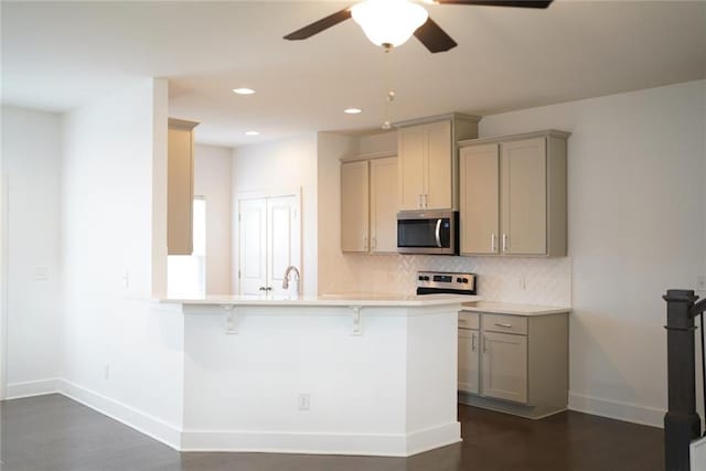 kitchen with stainless steel appliances, gray cabinetry, a breakfast bar, ceiling fan, and baseboards