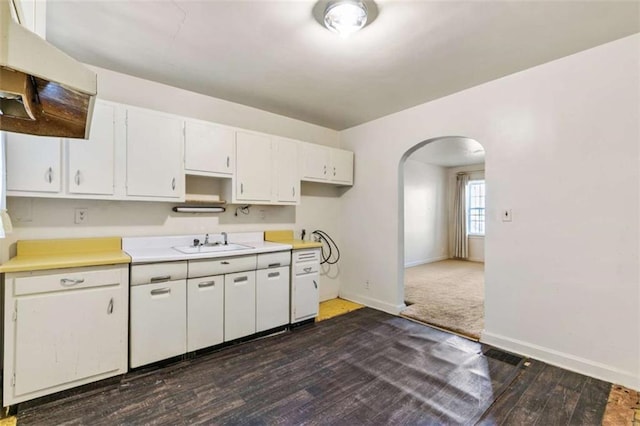 kitchen featuring a sink, arched walkways, light countertops, baseboards, and dark wood-style flooring