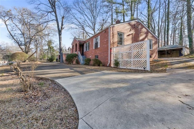 view of side of property with brick siding, concrete driveway, and a chimney