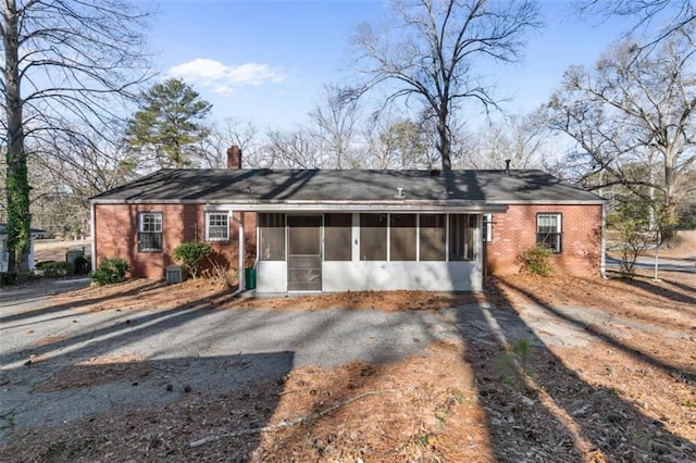 single story home featuring brick siding, central AC unit, a chimney, and a sunroom